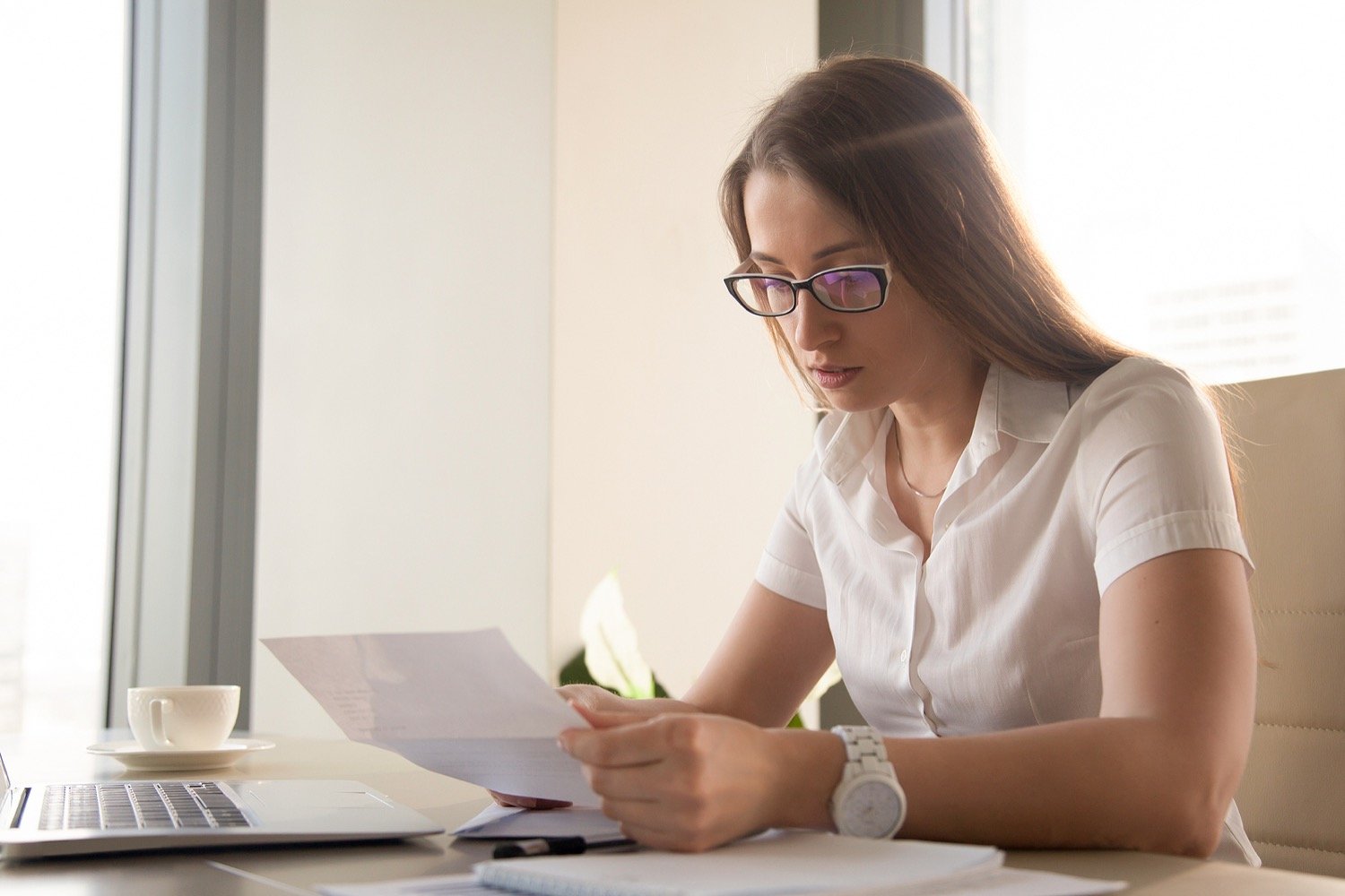 women with glasses behind laptop reviewing document